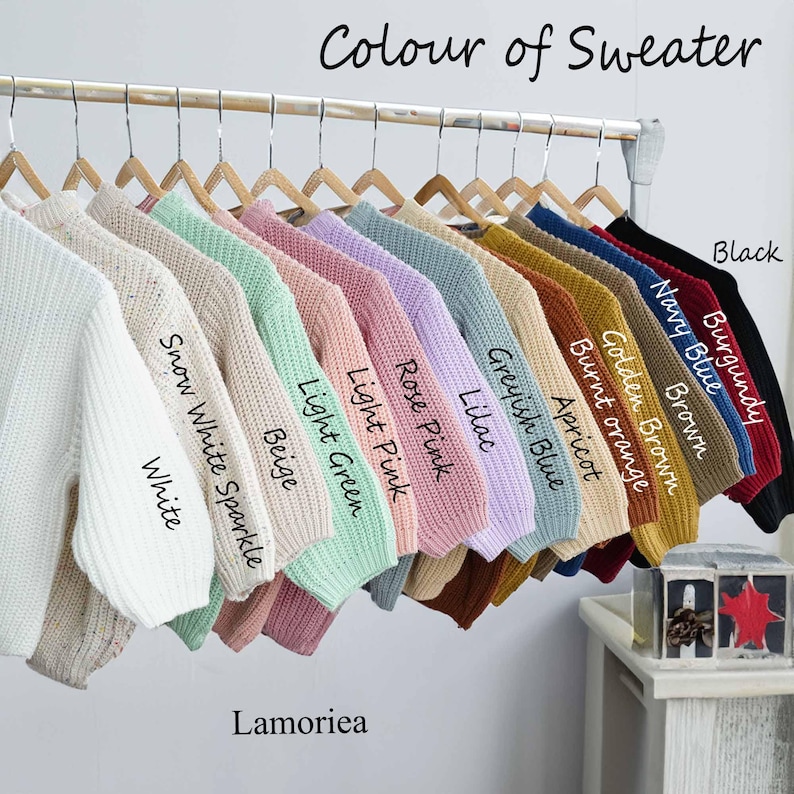 May include: A collection of knit sweaters hanging on a metal rack, labelled with colours including White, Snow White Sparkle, Beige, Light Green, Light Pink, Rose Pink, Lilac, Greyish Blue, Apricot, Burnt Orange, Golden Brown, Brown, Navy Blue, Burgundy, and Black.