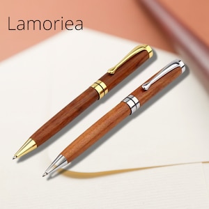 May include: Two wooden pens with gold and silver accents. The pens are on a white surface with a blurred background.
