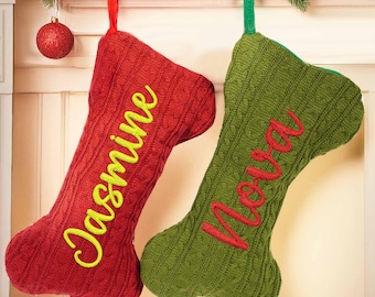 May include: Two Christmas stockings, one red with "Jasmine" in yellow script, the other green with "Nova" in red script. Both have a cable knit design and are hanging from a garland with red ornaments.