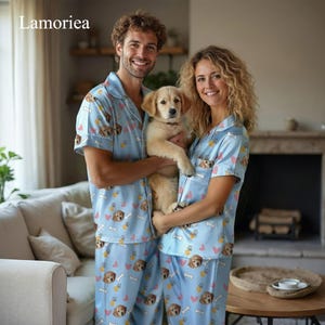 May include: Matching light blue pajama sets with a dog and paw print pattern. The sets include short-sleeved button-up shirts and pants. A couple holds a golden retriever puppy. The brand name "Lamorea" is in the top left corner.