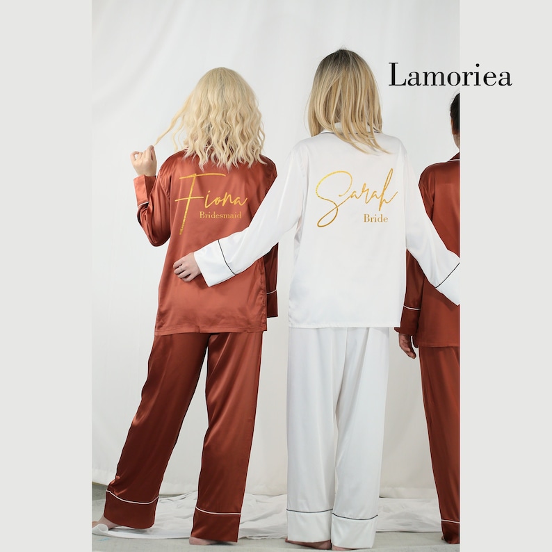 May include: Two-piece pajama sets in rust and white satin fabric with long sleeves and matching trousers. The rust set features the name Fiona and the word Bridesmaid in gold script. The white set features the name Sarah and the word Bride in gold.
