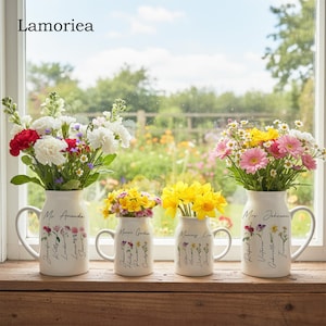 Könnte beinhalten: Vier weiße Keramikvasen mit Henkeln, jede gefüllt mit bunten Blumen. Die Vasen sind mit "Mr. Amanda", "Mama's Garden", "Mommy Lisa" und "Mrs. Johnson" beschriftet. Im Hintergrund ist ein Garten durch ein Fenster zu sehen.