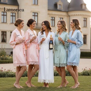 Puede incluir: Cinco mujeres con batas de satén en varios colores: rosa, blanco, verde menta y azul claro. Cada bata tiene un ribete de encaje y un nombre personalizado. Una mujer sostiene una botella de champán. La escena es al aire libre.