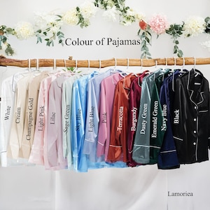 May include: A collection of long-sleeved button-down pajama shirts hanging on a wooden branch, labeled with colors: White, Cream, Champagne Gold, Light Pink, Lilac, Sage Green, Sky Blue, Light Blue, Pink, Terracotta, Burgundy, Dusty Green, Emerald Green, Navy Blue, and Black.