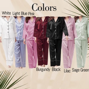 May include: A collection of seven button-down pajama sets with long sleeves and matching trousers, displayed in white, light blue, pink, burgundy, black, lilac, and sage green. Each set features a notched collar and contrasting piping detail.