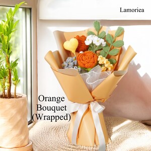 May include: A crocheted orange bouquet wrapped in brown paper with a white ribbon. The bouquet includes orange flowers, green leaves, and a yellow heart.