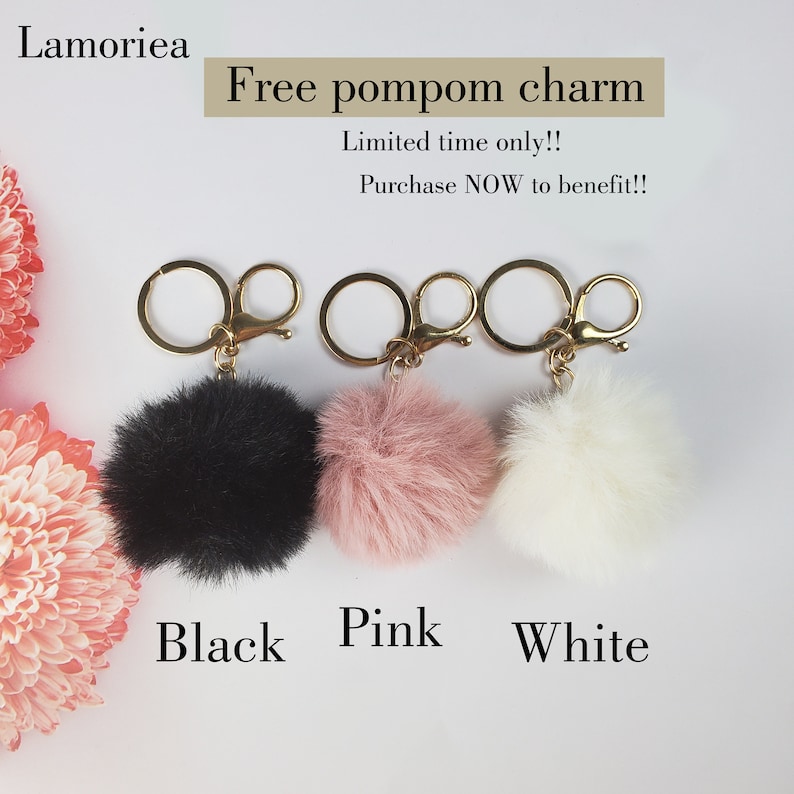 May include: Three pom-pom keychains in black, pink, and white. Each keychain has a gold metal ring and a lobster clasp.