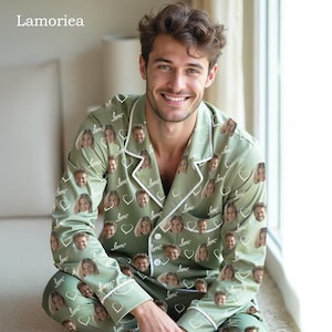 May include: Sage green pajama set with a white trim, featuring a repeating pattern of faces, hearts, and the word "love." The long-sleeved top has a notched collar and button-down front. The pajama bottoms are also visible.