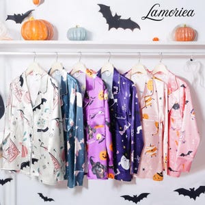 Peut inclure: Plusieurs chemises de pyjama sur le thème d'Halloween, dans des couleurs variées telles que le blanc, le bleu, le violet et le rose. Chaque chemise présente une impression unique avec des chauves-souris, des citrouilles et d'autres motifs effrayants. La marque "Lamoriea" est visible.