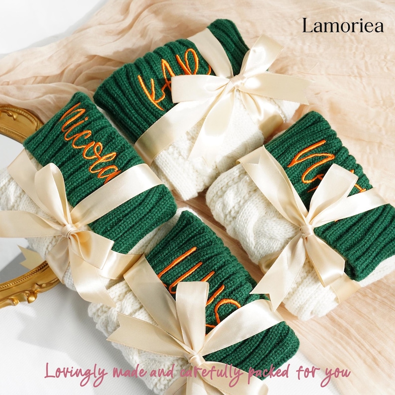 May include: Four personalized knitted gifts, each wrapped with a cream-colored ribbon. The gifts feature green and white sections, with embroidered names in orange. The text "Lamoriea" and "Lovingly made and carefully packed for you" are also visible.