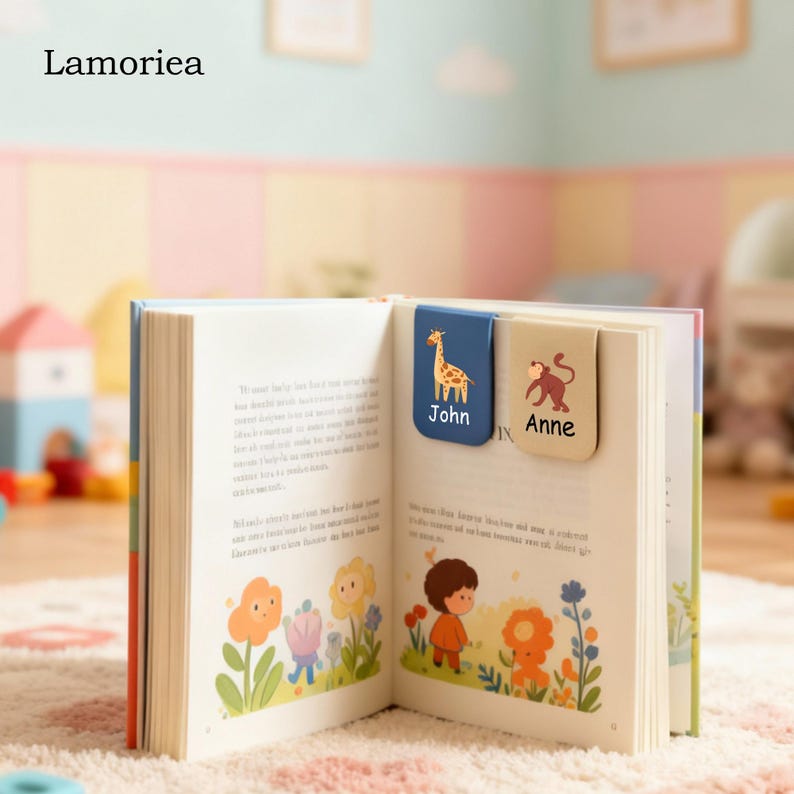 Puede incluir: Un libro abierto con dos marcadores magn&eacute;ticos. Un marcador es azul con una jirafa y el nombre "John". El otro marcador es beige con un mono y el nombre "Anne". La marca "Lamorirea" est&aacute; en la esquina superior izquierda.