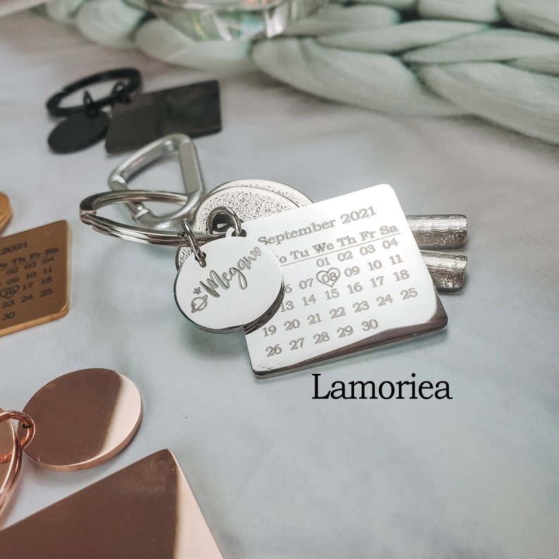 May include: Silver keyring with a calendar charm featuring the month of September 2021 and a small charm with the word "Megan" engraved on it. The keyring also includes a set of keys.