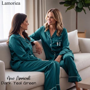 May include: A dark teal green pajama set featuring a long-sleeved button-down shirt with a collar and matching long pants. The shirt includes white piping along the edges and a small floral letter H embroidered on the chest pocket area.