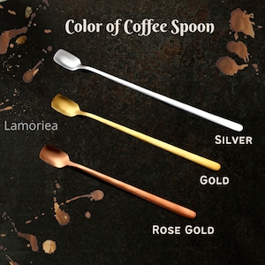 May include: Three coffee spoons in different colors: silver, gold, and rose gold. The spoons are laid out on a dark, textured surface.