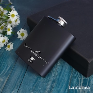 May include: Black metal flask with a silver cap and engraved text "Olivia 2023" with a graduation cap icon.