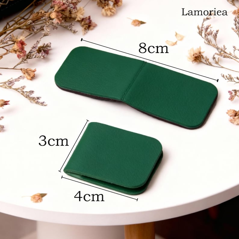 May include: Two green leather accessories, one rectangular (8cm long) and one square (4cm x 3cm), are displayed on a white surface. The accessories are likely small wallets or cardholders. The brand name "Lamoriea" is visible in the top right corner.