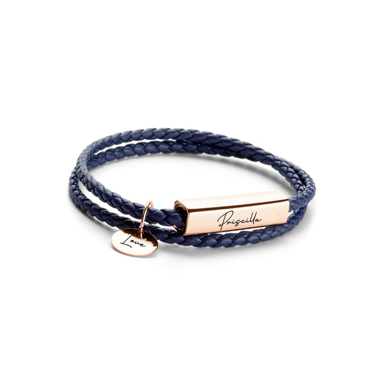 May include: A navy blue leather bracelet with a rose gold bar charm engraved with the name "Priscilla" and a smaller charm engraved with the word "Love".