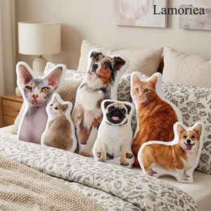 Puede incluir: Una colecci&oacute;n de cojines con tem&aacute;tica de mascotas que representan varias razas de perros y gatos. Los cojines muestran im&aacute;genes detalladas de un gato Sphynx, un gatito peque&ntilde;o, un pastor australiano, un pug, un gato atigrado naranja y un Corgi. Los cojines est&aacute;n colocados sobre una cama con ropa de cama con estampado floral.