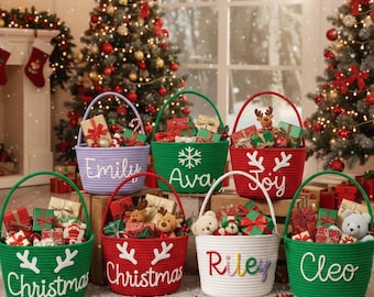 Op de afbeelding: Een verzameling kleurrijke, geweven kerstmandjes gevuld met ingepakte cadeaus en klein speelgoed. Elke mand is gepersonaliseerd met een naam of feestelijk woord zoals "Christmas" of "Joy". De manden hebben groene handvatten en staan voor versierde kerstbomen.