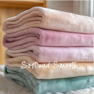 May include: A stack of five soft and smooth blankets in various pastel colors, including light pink, beige, and light blue. The blankets are folded neatly and arranged in a pile. The text "Soft and Smooth" is written in cursive on the bottom blanket.