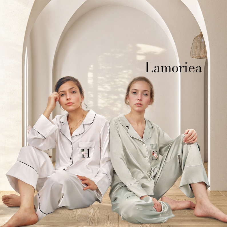 May include: Two sets of long-sleeved button-down pajamas with notched collars and contrasting piping. One set is white with a black letter H on the pocket, and the other is sage green with a black letter S on the pocket. The text Lamoriea is visible.