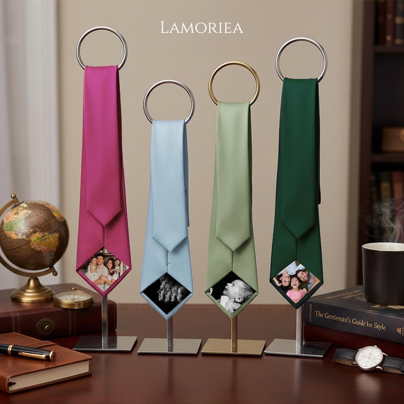 May include: Four neckties in magenta, light blue, sage green, and dark green, each hanging from a circular metal ring on a vertical stand. The bottom tip of each tie features a square photo insert displaying various family and portrait images.
