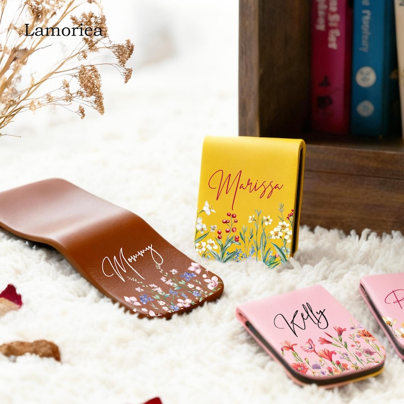 May include: A collection of personalized leather items, including a brown bookmark with floral accents and the word "Mommy", and several small, rectangular cases in yellow and pink, each with a name and floral design.