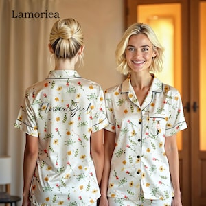 Può includere: Completo pigiama bianco con stampa floreale e rifiniture nere. La maglia a maniche corte ha una tasca e la scritta "Flower Girl" sul retro. Il pigiama presenta un motivo di fiori gialli e rossi.