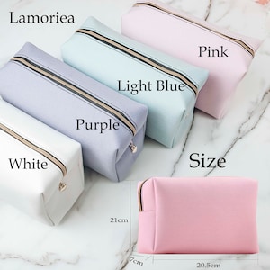 May include: Five zippered pouches in different colors: white, purple, light blue, and pink. The pouches are lined up in a row, with the white pouch on the left and the pink pouch on the right. The pouches are all the same size and have a black zipper. The text "Lamorilea" is at the top of the image. The text "Size" is below the pouches. The text "Purple" is below the purple pouch. The text "Light Blue" is below the light blue pouch. The text "Pink" is below the pink pouch. The text "White" is below the white pouch. The pink pouch is on a white surface with measurements in centimeters: 21cm, 7cm, and 20.5cm.