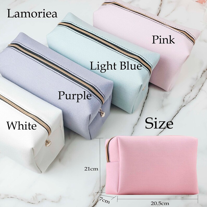 May include: Five zippered pouches in different colors: white, purple, light blue, and pink. The pouches are lined up in a row, with the white pouch on the left and the pink pouch on the right. The pouches are all the same size and have a black zipper. The text "Lamorilea" is at the top of the image. The text "Size" is below the pouches. The text "Purple" is below the purple pouch. The text "Light Blue" is below the light blue pouch. The text "Pink" is below the pink pouch. The text "White" is below the white pouch. The pink pouch is on a white surface with measurements in centimeters: 21cm, 7cm, and 20.5cm.
