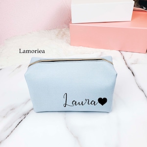 May include: Light blue zippered makeup bag with the name "Laura" and a black heart printed on the front.