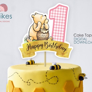 Puede incluir: Topper de pastel de Winnie de Pooh con un número uno de vichy rosa, un tarro de miel y las palabras "Feliz cumpleaños".