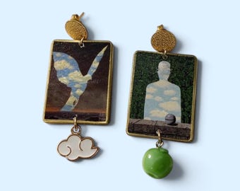 May include: A pair of rectangular drop earrings featuring gold-tone studs. One earring displays a bird silhouette filled with a blue sky and clouds, with a white cloud charm. The other shows a figure in a bowler hat, with a green apple charm.