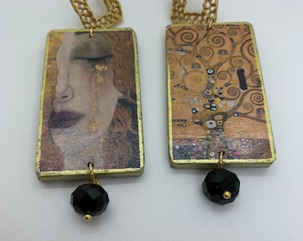 May include: A pair of gold-toned earrings with black crystal accents. Each earring features a rectangular pendant with a different image. One pendant features a painting of a woman's face with a tear, and the other pendant features a painting of a tree with swirling patterns.