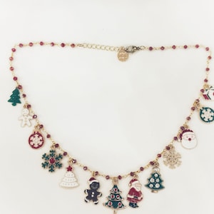 Könnte beinhalten: Eine goldene Halskette mit einer rot-grünen Perlenkette und mehreren Anhängern. Die Anhänger umfassen einen Lebkuchenmann, einen Weihnachtsbaum, eine Schneeflocke, einen Weihnachtsmann und eine Geschenkbox.