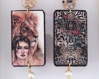 May include: A pair of rectangular drop earrings featuring a beige marbled stud. One earring displays a lion and a portrait of a person, while the other shows a leopard print pattern with roses. Each earring has a small white pearl dangling at the bottom.