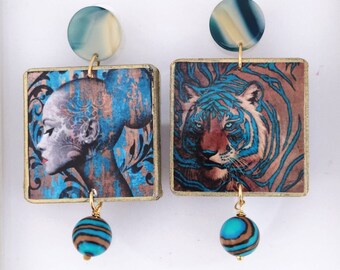 May include: A pair of dangle earrings featuring square pendants with gold-toned edges. One pendant displays a profile of a person with blue floral patterns, while the other shows a tiger. Each earring has a round blue-and-tan stud and a dangling bead.