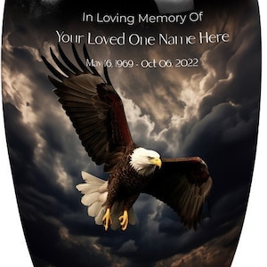 May include: Black cremation urn with a soaring bald eagle against a stormy sky backdrop. The urn is personalized with the text "In Loving Memory Of Your Loved One Name Here May 16, 1969 - Oct 06, 2022".