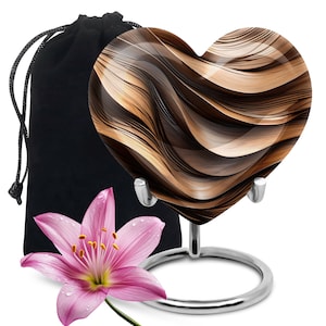 May include: A heart-shaped glass keepsake with a brown and gold abstract design, displayed on a silver stand. It comes with a black velvet pouch.