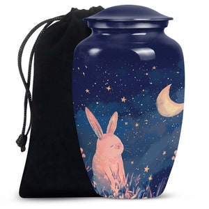 May include: A blue metal urn featuring a pink bunny rabbit illustration against a starry night sky background. The urn has a crescent moon and stars. It comes with a black velvet drawstring bag.