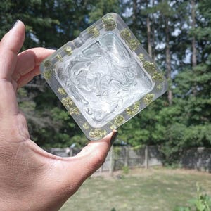 May include: A clear square ashtray with a swirl design and a green border. The border is made of small green pieces of resin.