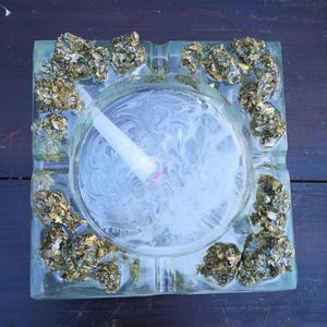 May include: A glass ashtray with a white swirl design and a green and gold leaf pattern around the edge.