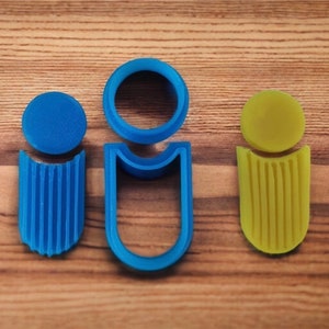 Peut inclure: Trois emporte-pièces en plastique en forme de personnes. L'un est bleu, l'autre jaune et l'autre bleu. Les découpoirs bleus ont une tête circulaire et un corps nervuré. Le découpoir jaune a une tête circulaire et un corps nervuré. Le découpoir bleu est en forme de U.