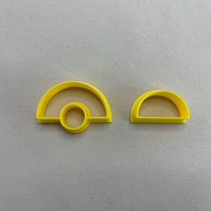 Peut inclure: Deux emporte-pièces en plastique jaune. L'un est un demi-cercle avec un cercle attaché, et l'autre est un demi-cercle plus petit. Les emporte-pièces sont conçus pour la pâtisserie et l'artisanat. Ils sont en plastique durable.