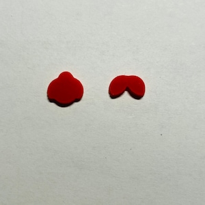 May include: Two small, red, abstract shapes are shown against a white background. One is a rounded, irregular form, and the other resembles a stylized moustache or bow. The objects appear to be made of a soft material.