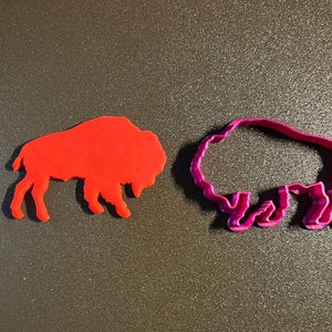 May include: Two cookie cutters in the shape of a buffalo. One is red and the other is pink.