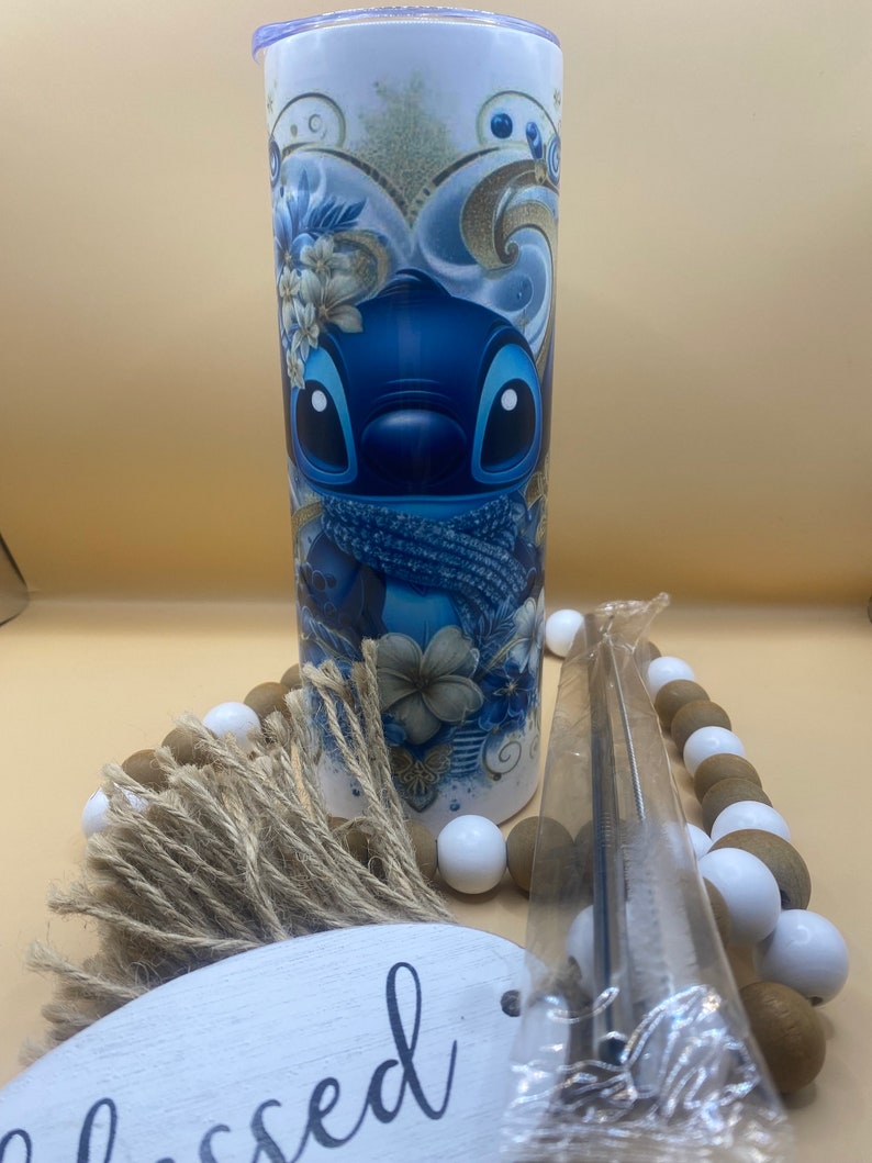 Puede incluir: Un vaso de acero inoxidable azul y blanco con un dise&ntilde;o de personaje de dibujos animados. El personaje es azul con ojos grandes y una bufanda azul. El vaso tiene una tapa blanca y una pajita.