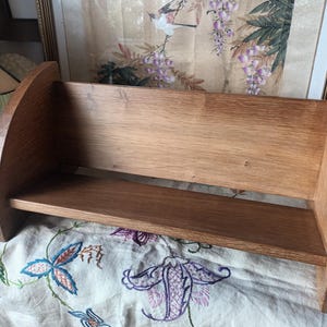 May include: A wooden bookshelf with a curved design. The shelf is made of light brown wood and has a simple, functional design. The shelf is sturdy and appears to be well-crafted, suitable for displaying books or decorative items. The overall aesthetic is rustic and classic.