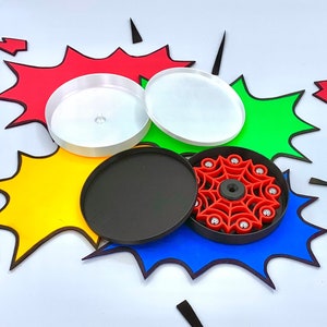 May include: A red and black fidget spinner with a spider web design. The spinner is surrounded by colorful paper cutouts.