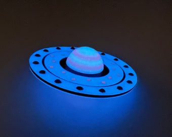 May include: A blue and white striped sphere with a pink ring around it, sitting on a blue and black circular base with a ring of black dots around the edge.